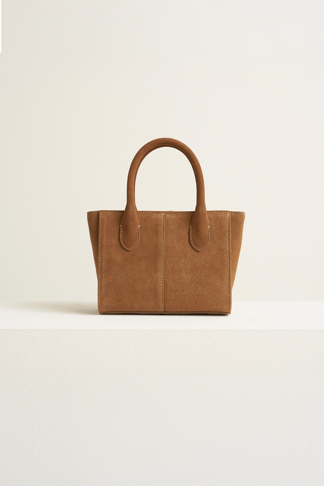 Small MIULIN Brunir suede bag with top handles and minimalist design, shown in natural light.