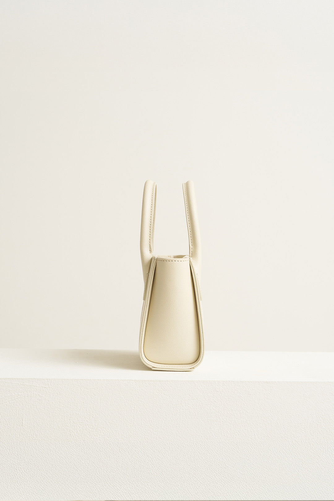 Small Ivoire leather bag by MIULIN featuring a sleek design and smooth ivory finish, with top handles and subtle stitching.