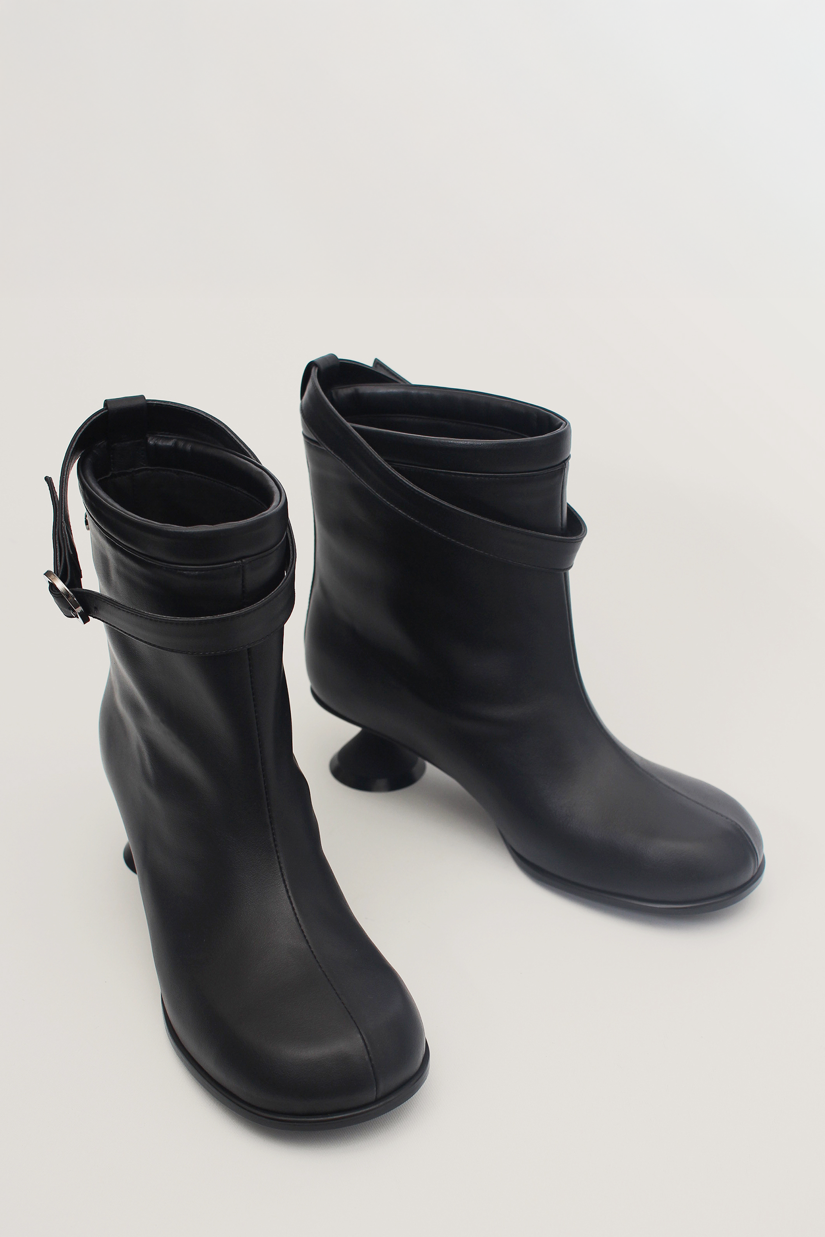 Black Uhjeo Hourglass Middle Heel Strap Boots by Finoacinque featuring ankle-high design and stylish strap details.