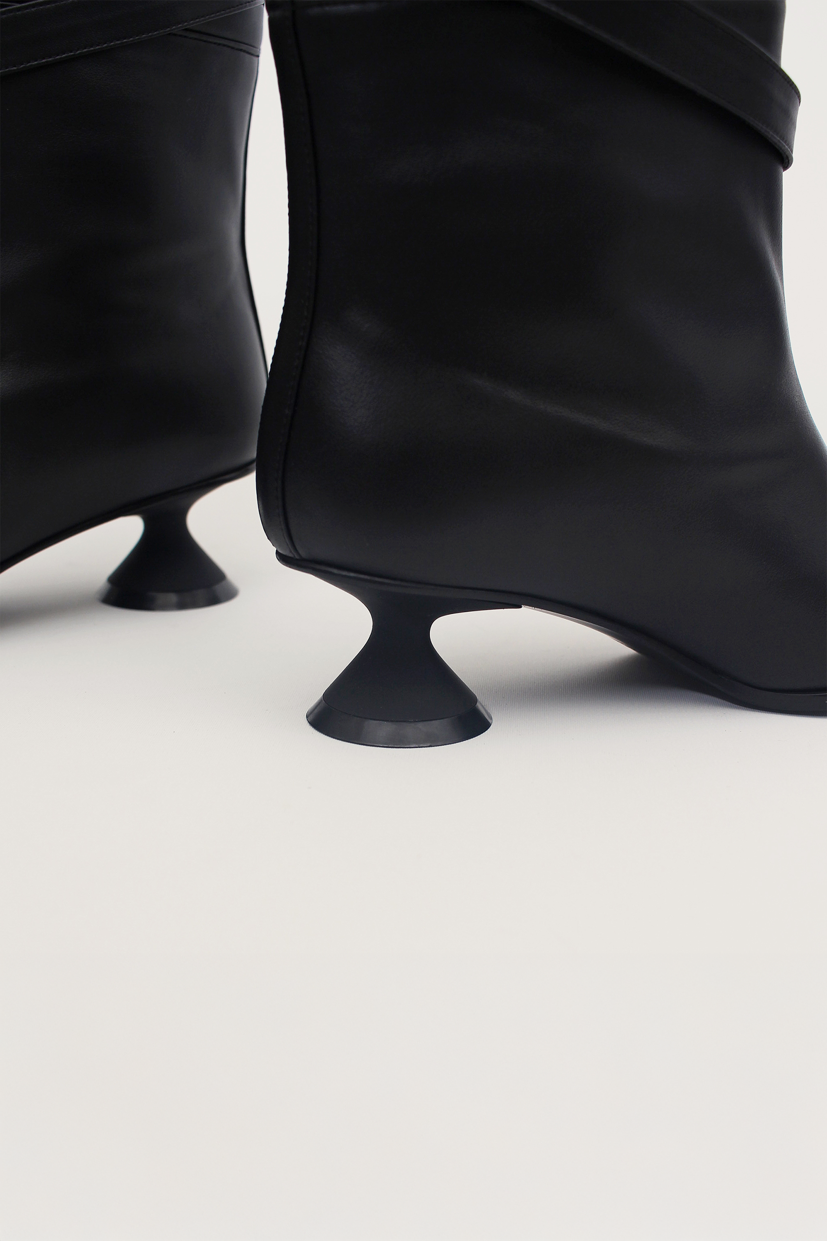 Black Uhjeo Hourglass Middle Heel Strap Boots by Finoacinque, featuring sleek design and ankle strap detail.