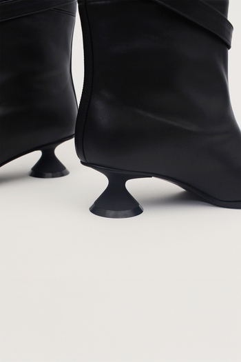 Black Uhjeo Hourglass Middle Heel Strap Boots by Finoacinque, featuring sleek design and ankle strap detail.