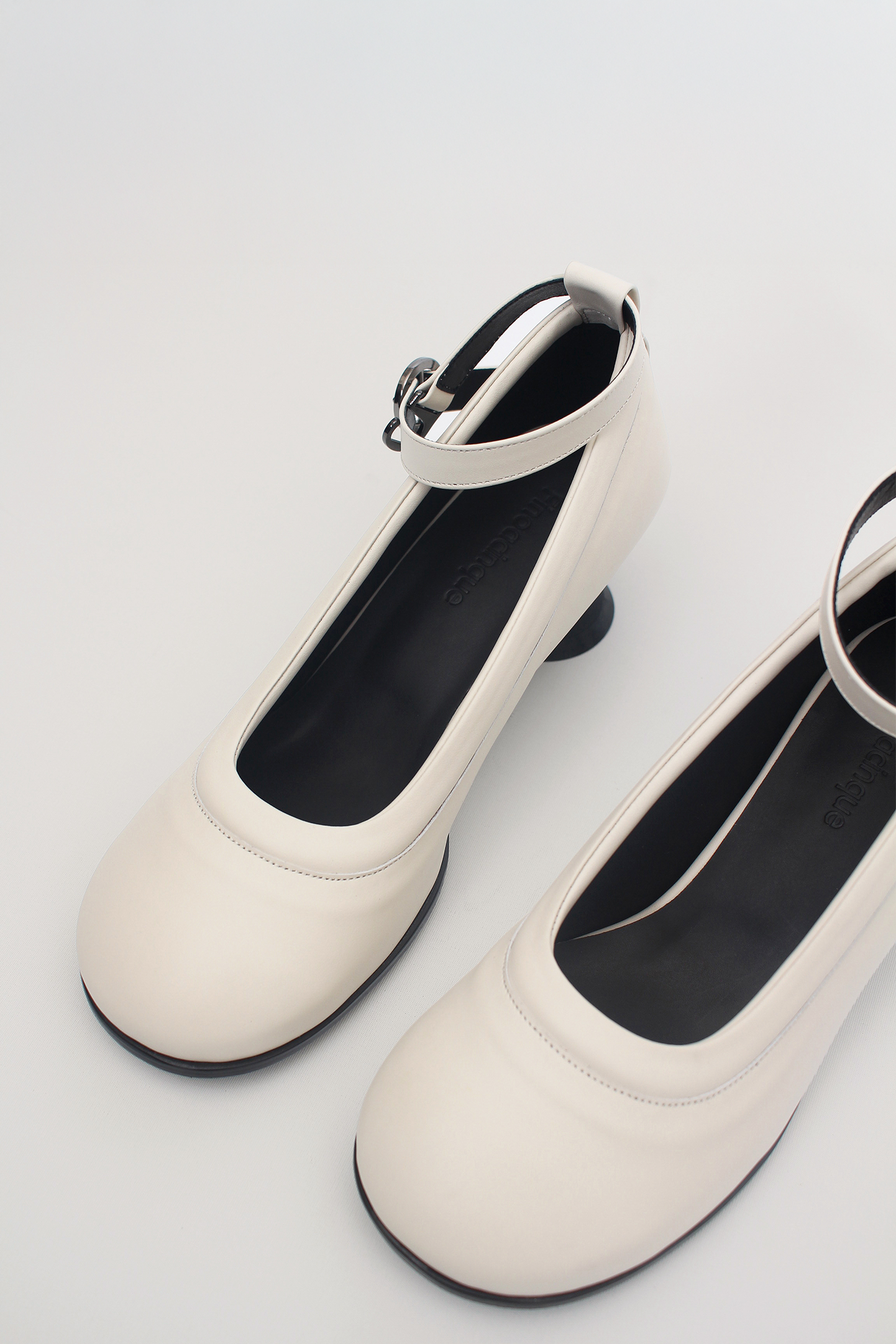 White Uhjeo Hourglass Middle Heel Strap Pumps by Finoacinque featuring a sleek design and ankle strap on a white background.