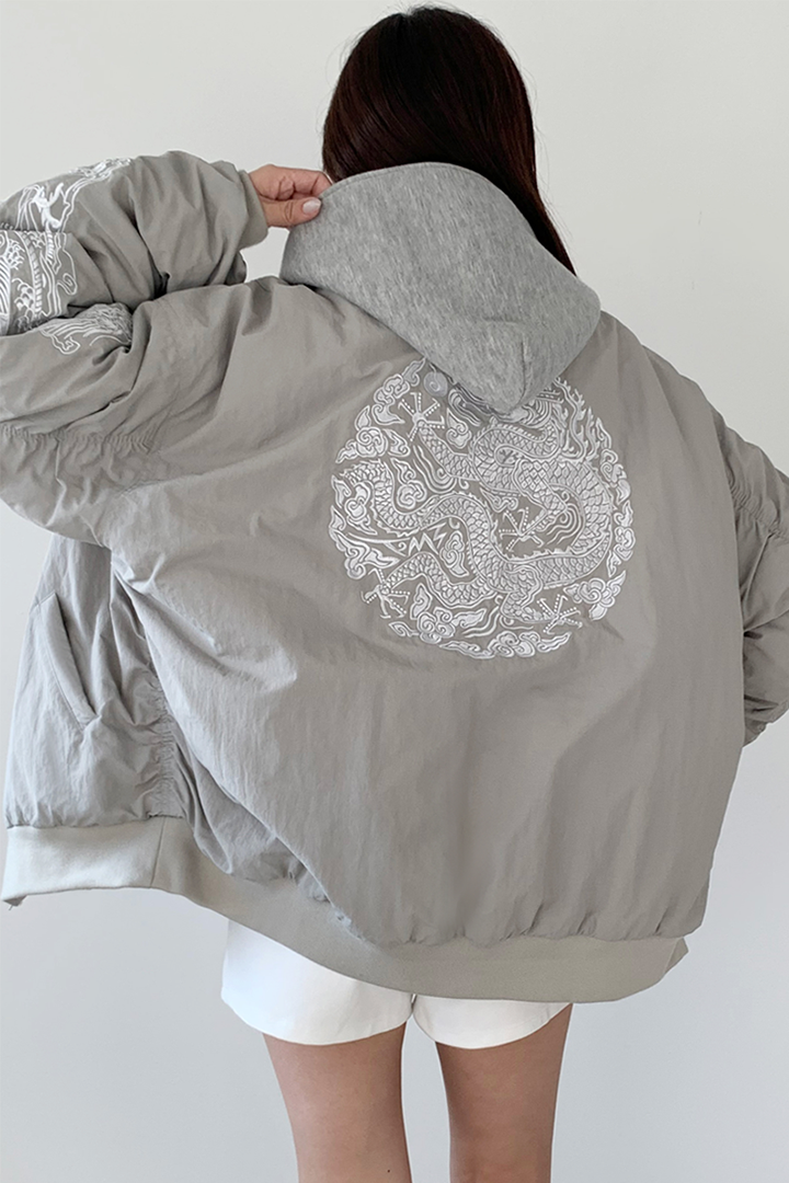 White bomber jacket by TM3 featuring beige and grey embroidery of a white dragon, made from lightweight fabric.